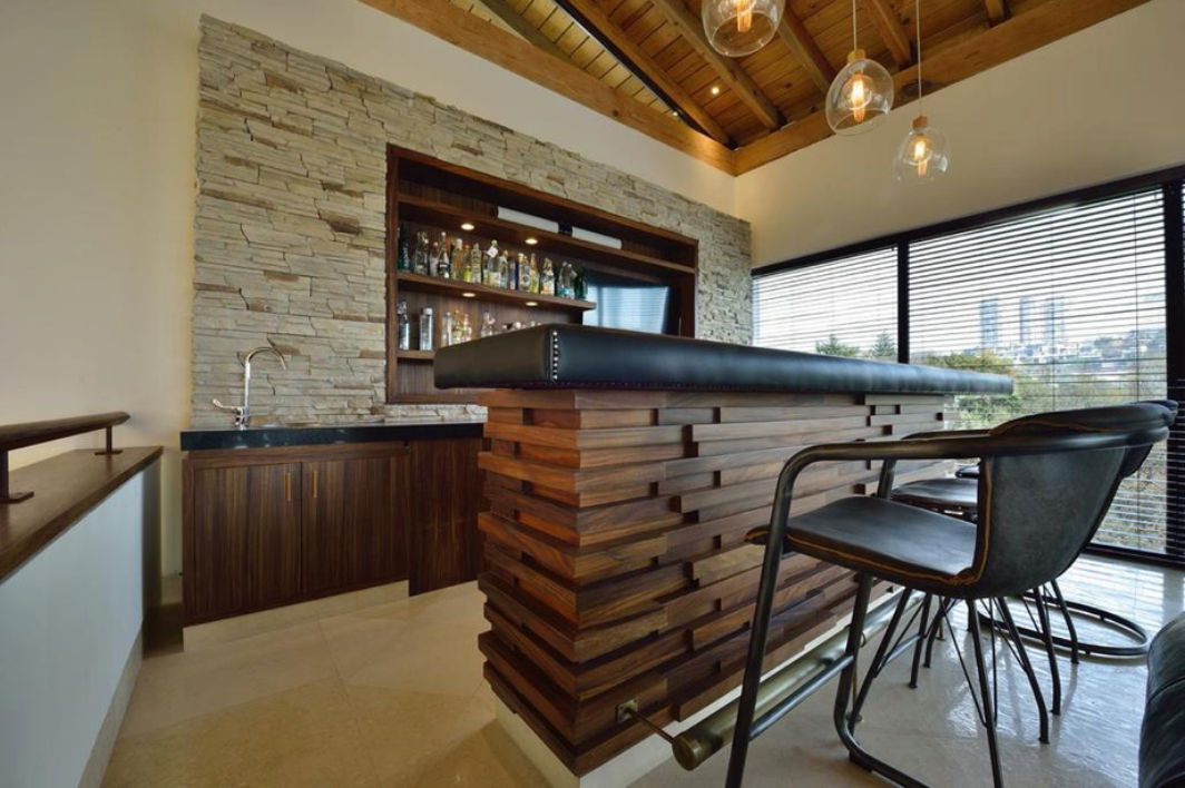 Interior residencial con barra de madera, muro de piedra y vista exterior.